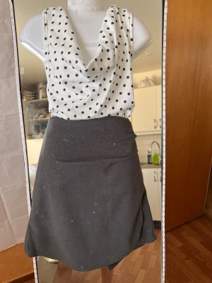 Set Vit prickig halter  ärmlös topp och kjol  - Säljer en vit ärmlös topp med svarta prickar och snygg draperad urringning. Toppen har en avslappnad passform och är perfekt för dig som gillar en lekfull men stilren look. Materialet känns mjukt och svalt, troligen bomull eller polyester.