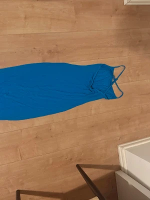 Blå lång klänning med smala axelband - Snygg blå långklänning med smala axelband och figurnära passform. Klänningen har en enkel och stilren design, perfekt för dig som gillar minimalistiskt mode. Materialet ser ut att vara mjukt och stretchigt för en bekväm känsla.