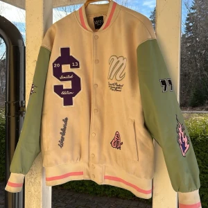 Oversized collegejacka - Beige typ college jacka med ljusgröna ärmar, rosa & svarta detaljer. Stängs med knappar och har ribbade muddar i rosa och beige. Oversized modell. Jättefint skick förutom att den blivit färgad inuti längst ner, se sista bilden. 