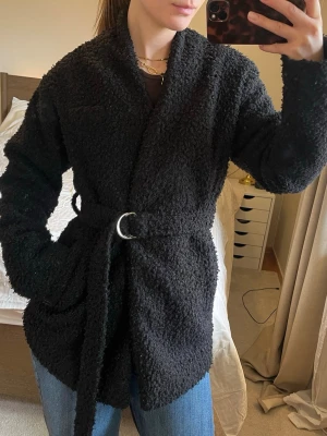 Svart teddyjacka - storlek 34 - Svart jacka / kappa i teddymaterial, två fickor och silvermedalj på skärpet - Nelly  Storlek 34/xs