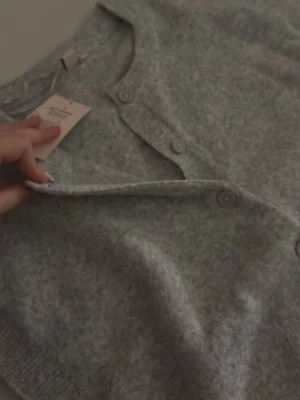 Ljusgrå stickad kofta från Nelly - Mysig ljusgrå stickad kofta/tröja från Nelly. Den kan användas som både kofta och tröja eftersom att det går att knäppa upp knapparna. Den är i helt nytt skick och har aldrig använts, den har även kvar prislappen. Den är verkligen jätte snygg men jag har inte fått någon användning av den. Den är i strl S