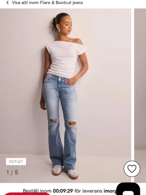 Ljusblå bootcut jeans med slitningar - Säljer ett par ljusblå bootcut jeans med slitna detaljer på knäna och klassiska fem fickor. Jeansen har en snygg flare nertill och fickor med lock bak. Perfekta för en avslappnad och trendig look.
