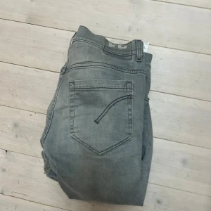 Gråa dondup jeans - Säljer ett par gråa jeans med rak passform och klassisk femficksdesign. Jeansen har normal midja och dragkedja med knapp framtill. Perfekta för en avslappnad och stilren look.