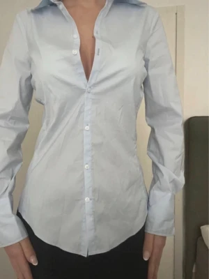 Figursyddd blå skjorta  - Snygg ljusblå skjorta från Zara med klassisk krage och knappar framtill. 