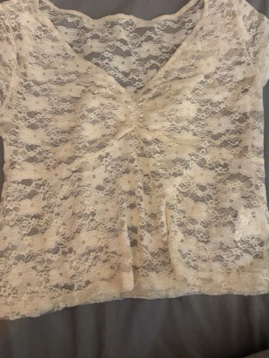 Vit spetsblus med v-ringning - Söt vit blus i spets med v-ringad hals och korta ärmar. Blusen har ett rynkat parti framtill som ger en fin detalj och är helt genombruten i spetsmaterial. Perfekt att styla med jeans eller kjol för en trendig look.