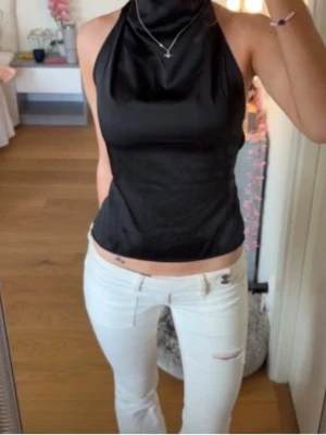 Svart halterneck topp med öppen rygg - Hör av dig för mer bilder❤️Säljer en svart halterneck topp med öppen rygg och snygga banddetaljer. Toppens material har en lätt glans och sitter tight över kroppen. Perfekt för dig som gillar en stilren och trendig look.