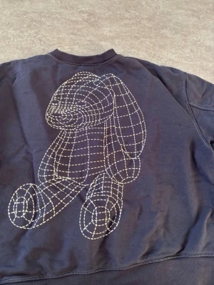 ZARA Unisex Sweatshirt, mörkblå storlek M - Riktig snygg och cool sweatshirt från Zara. Tröjan är boxig, med en modern passform för både män och kvinnor (unisex). Färgen är mörkblå med coola konstrastsömmar som ger en streetwear look. På baksidan är det en ”3D kanin” Storlek M Mycket fint skick. Djur- och rökfritt hem