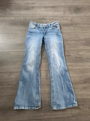 Blå utsvängda jeans från Gina Tricot - Säljer ett par ljusblå jeans från Gina Tricot med utsvängda ben och klassisk femficksmodell. Jeansen har slitna detaljer och är tillverkade i denim med en snygg tvätt. Perfekta för dig som gillar retrostil och vill ha ett par bekväma och trendiga jeans.