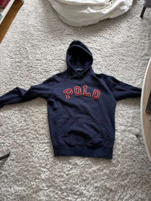  Ralph Lauren hoddie  - Snygg marinblå hoodie från Polo Ralph Lauren med stor röd POLO-text på bröstet. Klassisk känguruficka framtill och huva med dragsko. Tillverkad i mjukt bomullsmaterial som är perfekt för chill dagar eller streetwear-stil. Skriv vid funderingar eller frågor✌🏼
