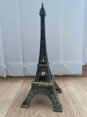 Eiffeltornet souvenir i metall - Säljer en detaljerad miniatyr av Eiffeltornet i metall med antik mässingsfinish. Tornet har texten PARIS längs ena sidan och är perfekt som inredningsdetalj eller samlarpryl. Ger en cool Paris-vibe till rummet och passar snyggt på hyllan eller skrivbordet.