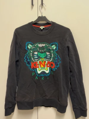 Svart Kenzo sweatshirt med tigertryck - Cool svart sweatshirt från Kenzo med ikoniskt broderat tigerhuvud i grönt, blått och rött på bröstet. Rund halsringning