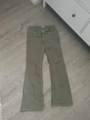Olivgröna bootcut jeans från Nelly - Snygga olivgröna jeans från Nelly med bootcut-modell och klassisk femficksdesign. Jeansen har hög midja och stängs med knapp och dragkedja. Perfekta för dig som vill ha en trendig och avslappnad look.