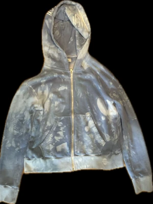 Blå tie-dye zip hoodie från Deema - Snygg blå zip hoodie från Deema med tie-dye mönster och broderad logga på ärmen. Hoodien har dragkedja framtill, känguruficka och ribbade muddar. Perfekt för en chill och avslappnad stil. Cropped fit.
