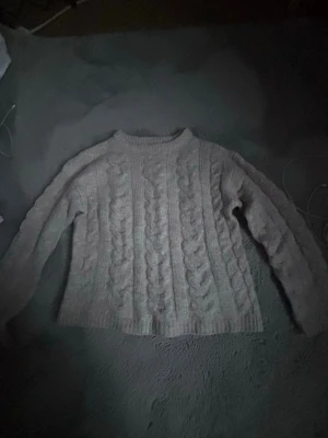 Beige kabelstickad tröja 157 XS - Mysig beige kabelstickad tröja från 157 med rund hals och ribbade muddar. Tröjan har ett klassiskt flätmönster och är perfekt för kalla dagar. Långärmad och i mjukt material som känns skönt mot huden.
