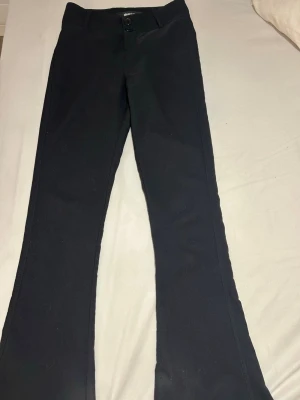 Svarta bootcut byxor  - Snygga svarta bootcut/kostym byxor med två bakfickor. Klassisk design med knapp och dragkedja framtill. Materialet är stretchigt och bekvämt, perfekt för en trendig look. Passar till många olika stilar.