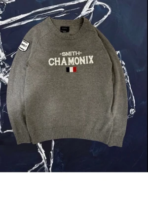 Grå stickad tröja Smith Chamonix - Snygg grå stickad tröja från Smith med texten 'CHAMONIX' och en liten fransk flagga framtill. Tröjan har rund hals, ribbade muddar och en patch på ena ärmen. Tröjan är liten i storlek, står M men passar bäst för dig som har S. Bara hör av dig om du har några frågor! 