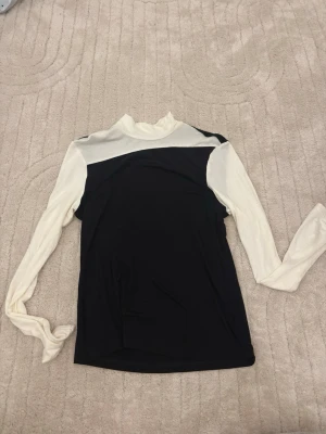 Svart och vit långärmad tröja - Snygg långärmad tröja i svart och vitt med kontrastpaneler. Toppen är tillverkad i ett stretchigt material som sitter tajt mot kroppen. 