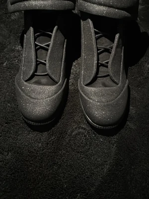 Maison margiela futures black glitter - Säljer ett par svarta sneakers med glittrigt material och breda kardborreband runt ankeln. Skorna har en chunky design och är riktigt statement med sin unika look. Perfekta för dig som vill sticka ut och gillar coola detaljer.