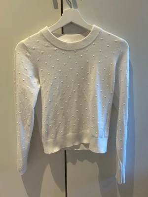 Vit stickad tröja med strukturmönster - Säljer en vit stickad tröja med små upphöjda prickar över hela plagget. Tröjan har rund halsringning, långa ärmar och ribbade muddar vid ärmslut och nederkant. Perfekt för dig som gillar en enkel men ändå unik stil.