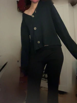 Svart oversized kofta med knappar - Säljer en svart oversized kofta med stora dekorativa knappar framtill. Koftan har en avslappnad passform, långa ärmar och är gjord i ett mjukt stickat material. Perfekt för lager på lager och en chill look.