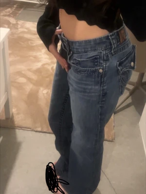 Blå bootcut jeans med låg midja - Säljer ett par blå bootcut jeans med låg midja och klassiska fem fickor. Jeansen har en snygg tvättad look och vida ben. Perfekta för dig sop needed en relaxed och trendig stil. Inget synligt märke på jeansen. Köpte dom i london, jeansen är inte alls använda nästan helt nya och hade prislapp när jag köpte dom. Nypris: 1499kr