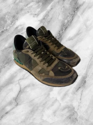 Valentino camo sneakers i grönt - Snygga sneakers från Valentino med camo-mönster i olika nyanser av grönt och brunt. Skorna har gröna skosnören, svarta detaljer och en klassisk låg siluett. Materialmix av mocka och textil ger en cool och exklusiv känsla.