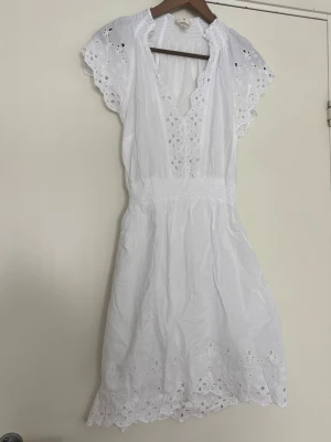 Vit broderad sommarklänning H&M - Söt vit kortklänning från H&M i bomull med broderade spetsdetaljer och v-ringning. Klänningen har korta ärmar med volang och vackra hålbroderier längs kanterna. 