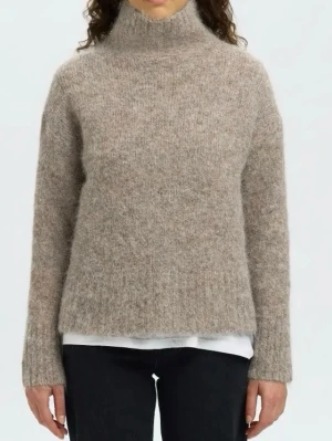 Beige stickad polotröja - Mysig beige stickad polotröja med lång ärm och rak passform. Tröjan har hög krage och är tillverkad i ett fluffigt material som ger en avslappnad look. Perfekt för kalla dagar och enkel att matcha med olika outfits.