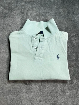 Ljusgrön pikétröja från Ralph Lauren - Klassisk ljusgrön pikétröja från Ralph Lauren med broderad logga på bröstet. Tröjan har krage, knappar framtill och är tillverkad i bomull för en bekväm känsla. Perfekt till jeans eller shorts för en avslappnad men snygg look. Längd 60 cm bredd 42. Priset kan diskutera och om du har några frågor det är bara och skriva 😊