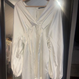 Vit satinklänning med v-ringning - Snygg vit satinklänning från gina tricot med v-ringning och långa puffärmar. Den är helt oanvänd med prislappen kvar. Den är från förra året så den säljs inte längre