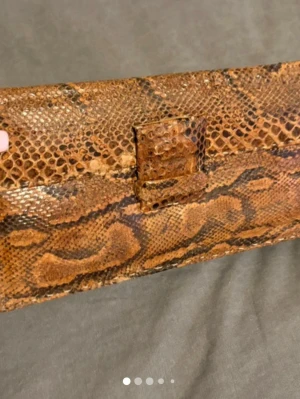 Brun kuvertväska i ormskinnsmönster - Snygg brun kuvertväska med ormskinnsmönster och rektangulär form. Väskan har ett spänne framtill