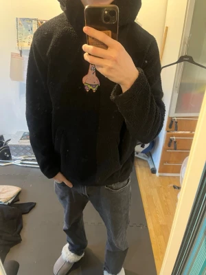 Svart fleecehoodie med Patrick-motiv - Mysig svart hoodie i fleece med en broderad Patrick från Svampbob på bröstet. Hoodien har stor huva och magficka framtill. 