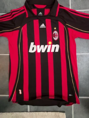 AC Milan matchtröja Kaka #22 Adidas - Säljer en klassisk AC Milan matchtröja från Adidas med Kaka och nummer 22 på ryggen. Tröjan är röd och svart med gulddetaljer, klubbmärke och Bwin som sponsor på bröstet. Perfekt för dig som älskar fotboll och vill ha en ikonisk supportertröja. Storleken är mer som L. Priset är ej hugget i sten! 