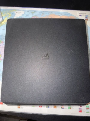 Sony PlayStation 4 Slim konsol - Säljer en svart PlayStation 4 Slim från Sony. Konsolen har en stilren, matt finish och är kompakt och tunn i formen. Perfekt för gaming och streaming, med klassisk PS4-design och logotyp på ovansidan.