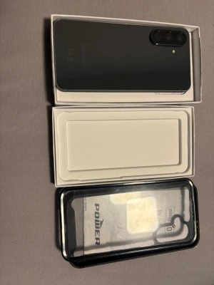 Samsung Galaxy svart Android-telefon - Snygg svart Samsung Galaxy Android-telefon med stilren design och rundade hörn. Baksidan är slät och har trippelkamera med LED-blixt. Telefonen levereras i originalkartong och ett genomskinligt skal medföljer. Perfekt för dig som vill ha en modern och kraftfull mobil.