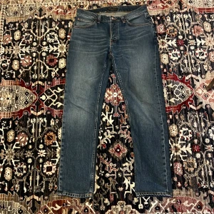 Nudie jeans - Säljer ett par klassiska blå jeans från Nudie Jeans med rak passform. Jeansen har orange kontrastsömmar och knappgylf. Storlek 32/32 osäker på modell men tror grim tim. Typ helt nya går gärna mer i pris.