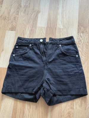 Svarta high waist shorts i bomull - Snygga svarta shorts med hög midja och uppvikta benslut. Klassisk femficksmodell med knapp och dragkedja framtill. Tillverkade i mjuk bomull, perfekta för varma dagar.