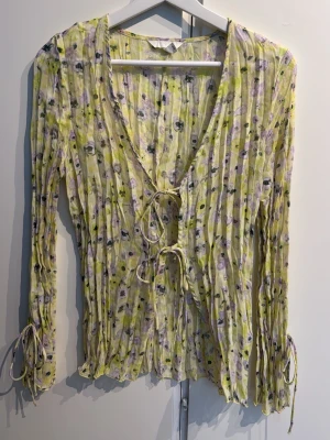 Blus med knytning - Söt blus i gul nyans med blommigt mönster i lila och svart. Så fin över en bikini eller topp under, endast använd ca 2ggr! Knytning fram till och på ärmarna