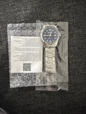 Silverfärgad klocka från Geneva - Stilren klocka från Geneva med blå urtavla och datumvisning. Armbandet är i blankt silverfärgat metall och har klassisk länkdesign. Urtavlan har tydliga siffror och markeringar, vilket gör den enkel att läsa av. Perfekt accessoar för dig som gillar en clean look.