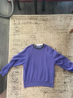 Lila sweatshirt från Acne Studios - Snygg lila sweatshirt från Acne Studios med rund halsringning och svart/vit logotypdetalj runt kragen. Tröjan är väldigt oversized