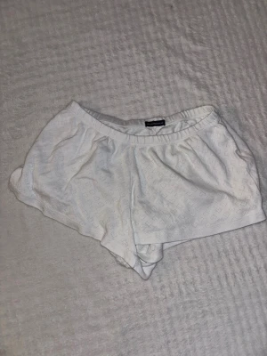 Vita Brandy Melville bomullsshorts - Säljer ett par vita shorts från Brandy Melville i mjuk bomull med elastisk midja. Shortsen har ett diskret hålmönster som ger en söt och luftig känsla, perfekta för varma dagar. 