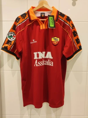Roma retro matchtröja 98 / 99 - Totti #10 - L - Säljer en retro matchtröja / fotbollströja för Roma säsong 1998 / 1999 med Totti #10 på ryggen och serie a patch på armen. Tröjan är en reprint helt ny och oanvänd. Storlek L.