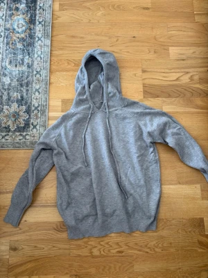 Grå basic hoodie med dragsko - En enkel och stilren grå hoodie med huva och dragsko. Tillverkad i mjukt material som känns skönt mot huden. Perfekt för chill dagar eller när du vill ha en avslappnad look. Ribbstickade muddar vid ärmslut och nederkant.