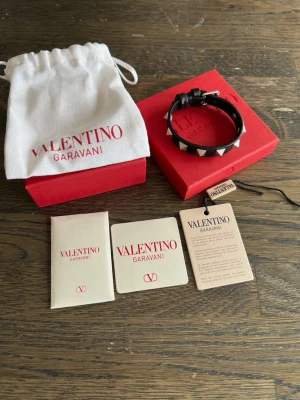 Valentino Garavani svart nitarmband - Snyggt svart läderarmband från Valentino Garavani med silverfärgade pyramidnitar och justerbart spänne. Kommer med original ask, dustbag och äkthetskort. 