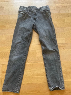 Grå/svarta raka jack and jones jeans i klassisk modell - Säljer ett par grå/svarta jeans med rak passform och fem fickor. Det är jack and jones jeans jom jag har växt ut W30 L32