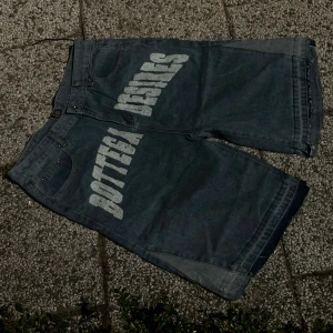 Blå jeansshorts med tryck från bottega Desires - Säljer ett par blå jeansshorts från bottega  Desires med stort vitt tryck på framsidan. Shortsen har klassisk femficksdesign och normal passform. Perfekta för dig som vill sticka ut med en unik streetwear-look.