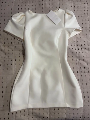 Vit Kort Klänning Zara (Helt Ny) - Kort vit klänning från Zara. Helt ny med lapp. Vit/cream färg med puffiga ärmar och slät material. Perfekt till studenten. Classy och chic. Storlek M. 