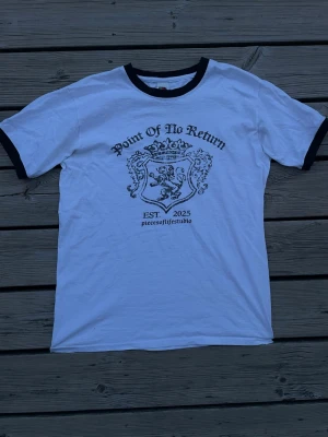 Fet t-shirt - Säljer en vit t-shirt med svart text 'Point Of No Return' och ett lejonmotiv på bröstet. Svarta kontrastkanter vid hals och ärmslut ger en retrovibe. En fet tisha helt enkelt, fråga vid fundering så tar vi det därifrån👍!! obs‼️det står S men sitter mer som en XS
