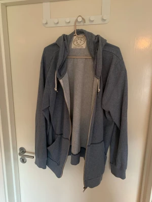 Grå zip hoodie med fickor - En klassisk grå zip hoodie från Urban Outfitters med huva. Hoodien har två stora fickor framtill. Tillverkad i mjukt bomullsmaterial. 