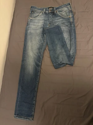 Blå slim fit jeans från Jack & Jones  - Snygga blå slim fit jeans från Jack & Jones  med klassisk femficksdesign och diskreta slitningar framtill och baktill. Jeansen har normal midja, smal passform och är tillverkade i denim med lätt stretch för extra komfort. Perfekt för att matcha till de mesta. Strl W30 L32